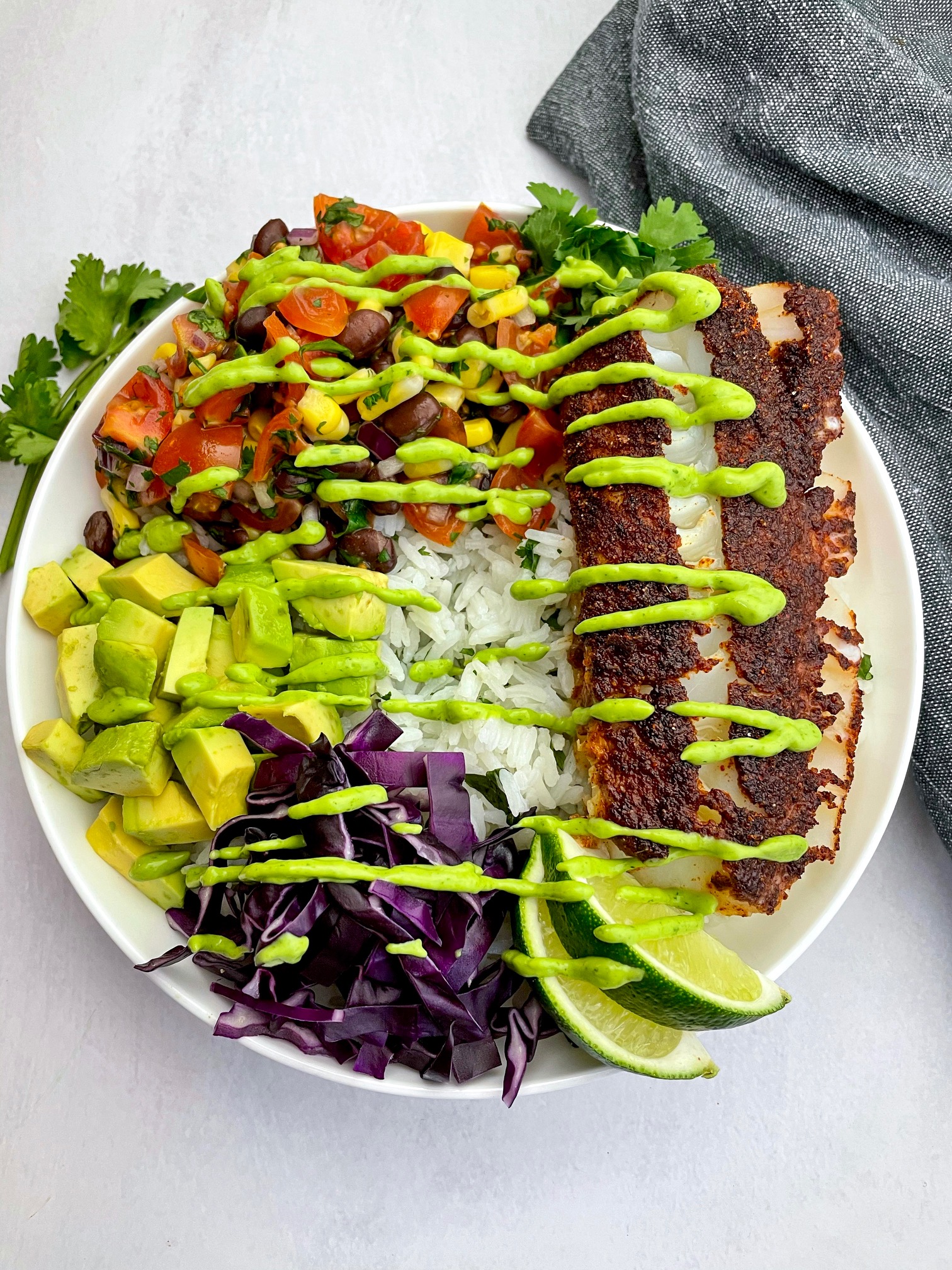 a spicy fish taco bowl with rice, salsa, avocado, red cabbage and a avocado crema
