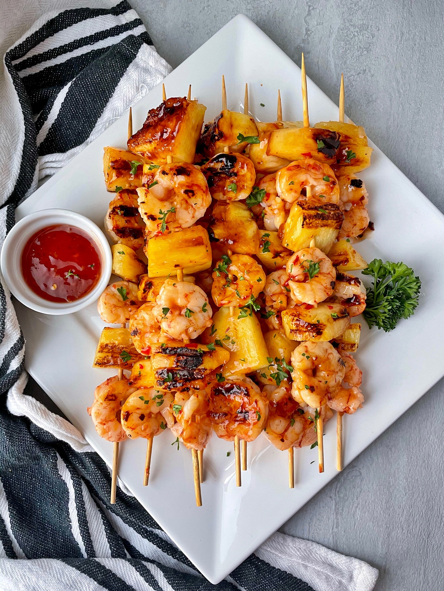 a plate of pineapple shrimp skewers with a side of sauce