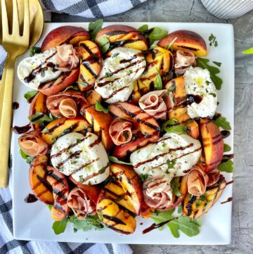 a serving plate with peach burrata and prosciutto salad with a balsamic drizzle