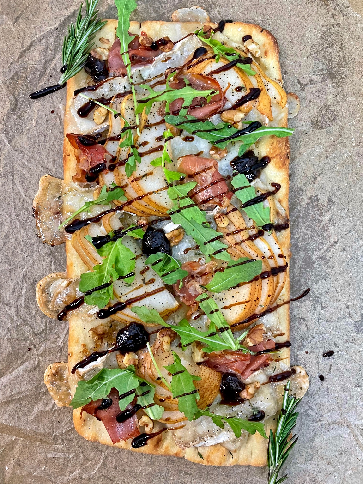 a flatbread with pear, brie, prosciutto, walnuts, arugula and balsamic glaze