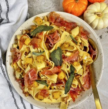 a bowl of pumpkin pappardelle with brown butter garnished with crispy sage with a serving spoon