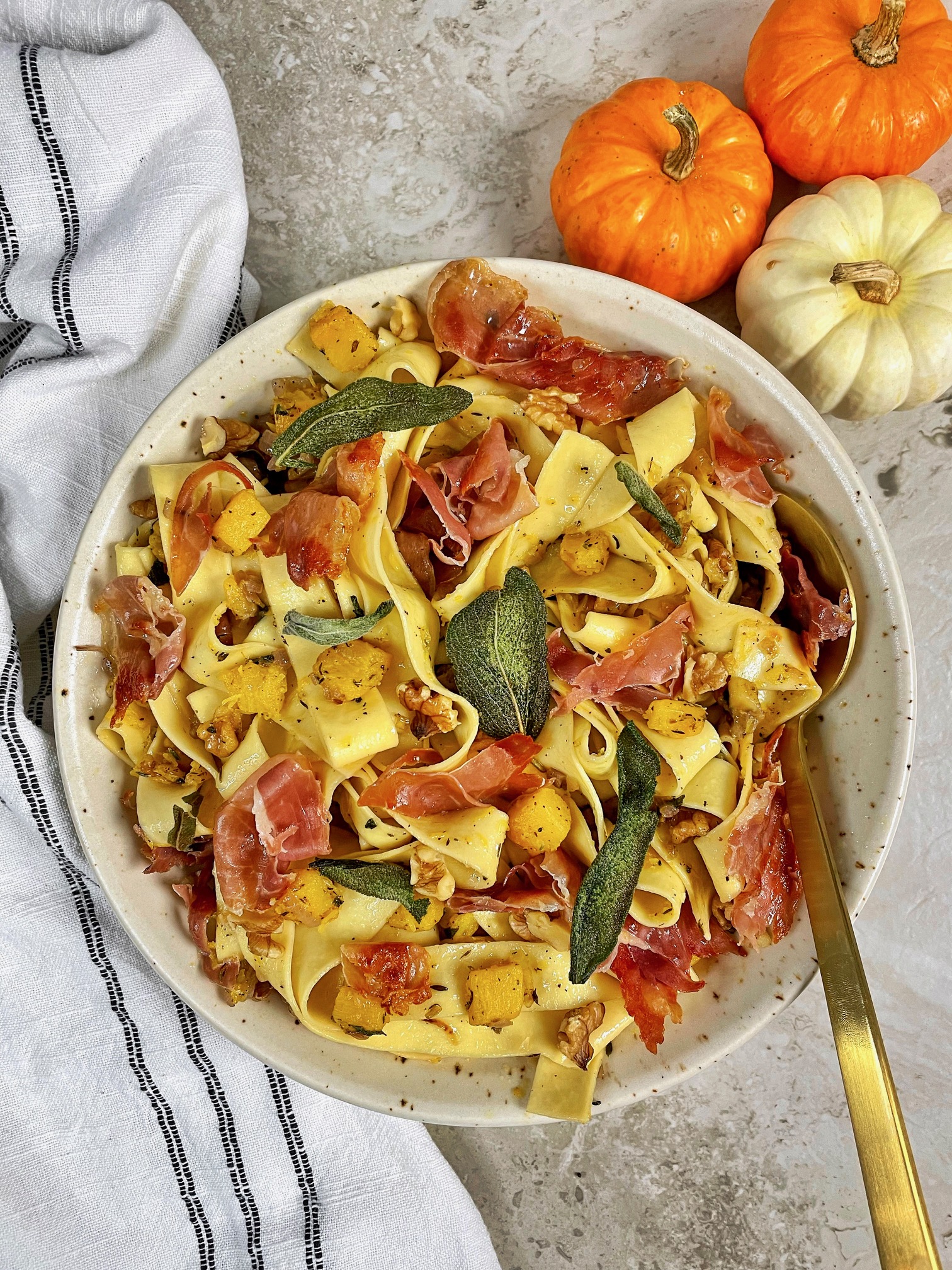 a bowl of pumpkin pappardelle with brown butter garnished with crispy sage with a serving spoon