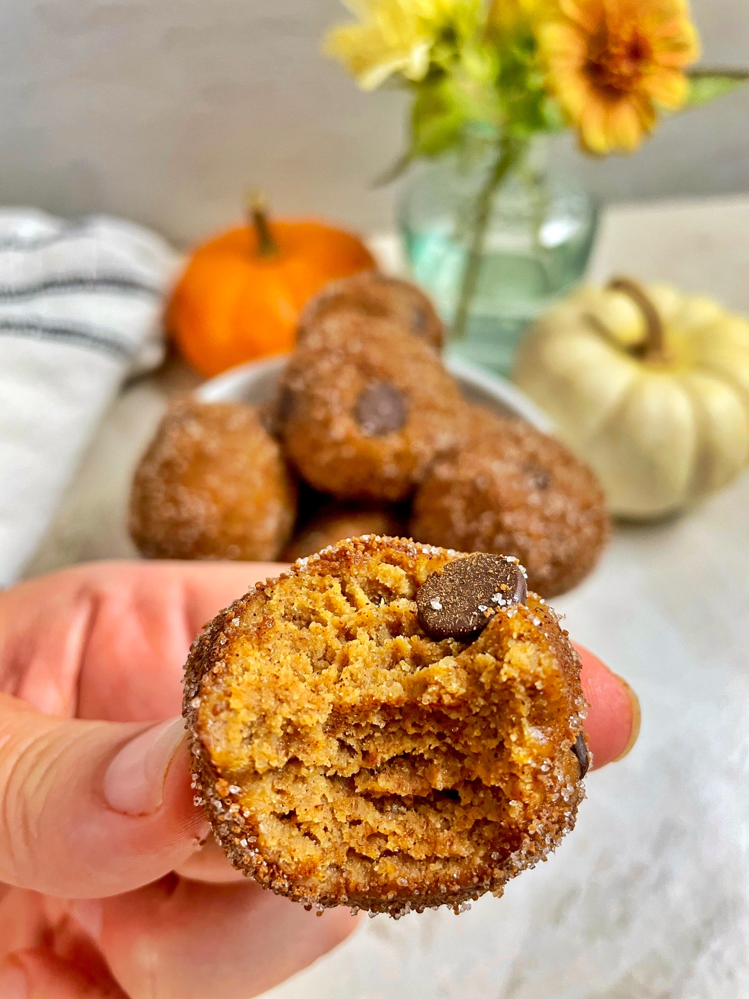 a pumpkin cookie dough bite coated with cinnamon sugar with a bite taken out of it to show the texture inside