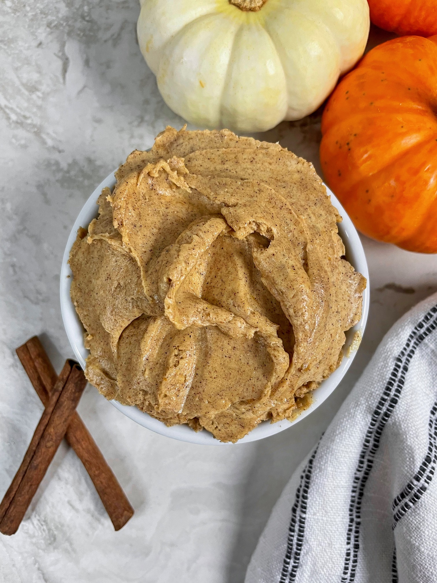 a ramekin of whipped pumpkin honey butter with pumpkins and cinnamon sticks around it