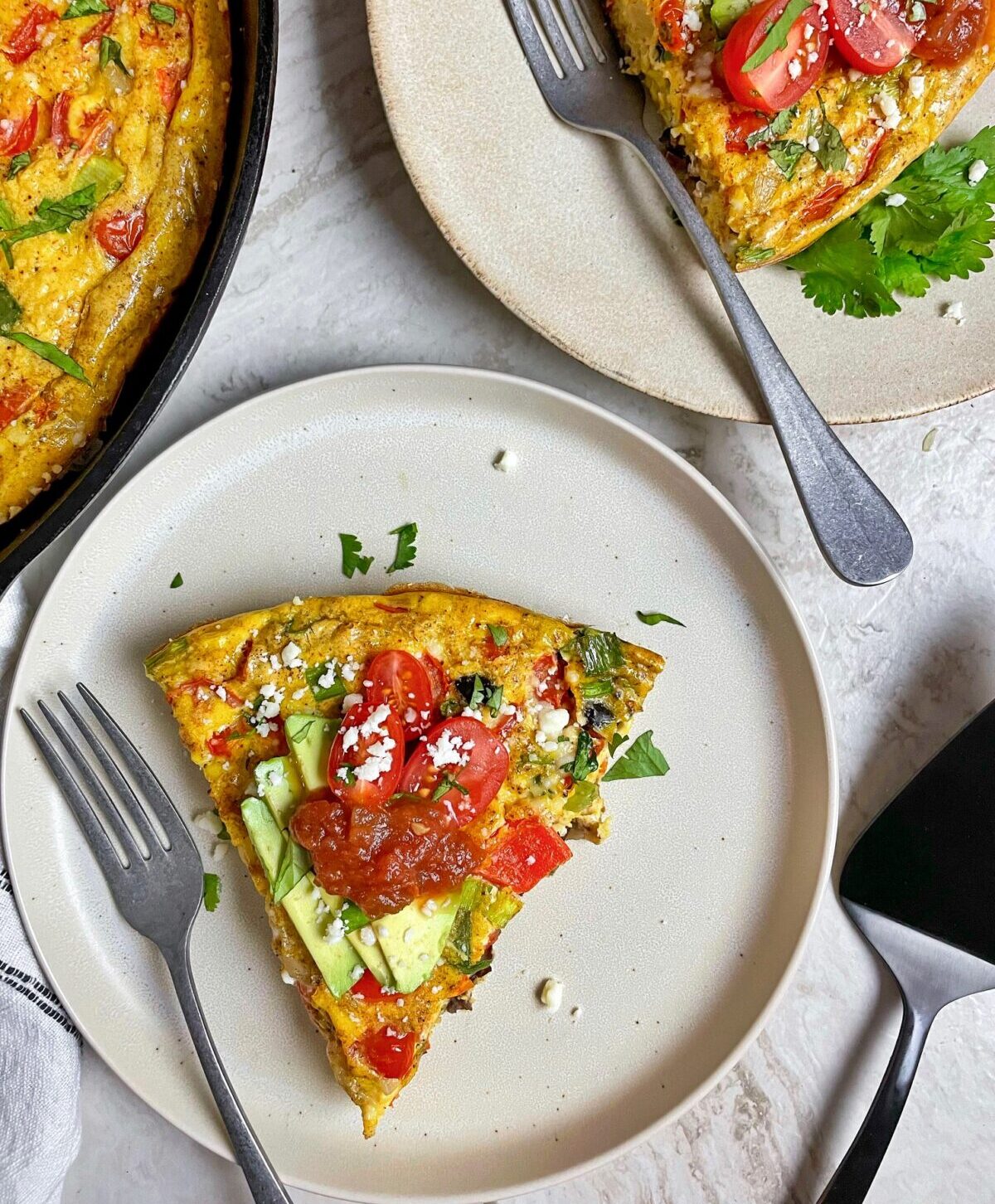 two slices of frittata on plates with the pan of frittata to the left