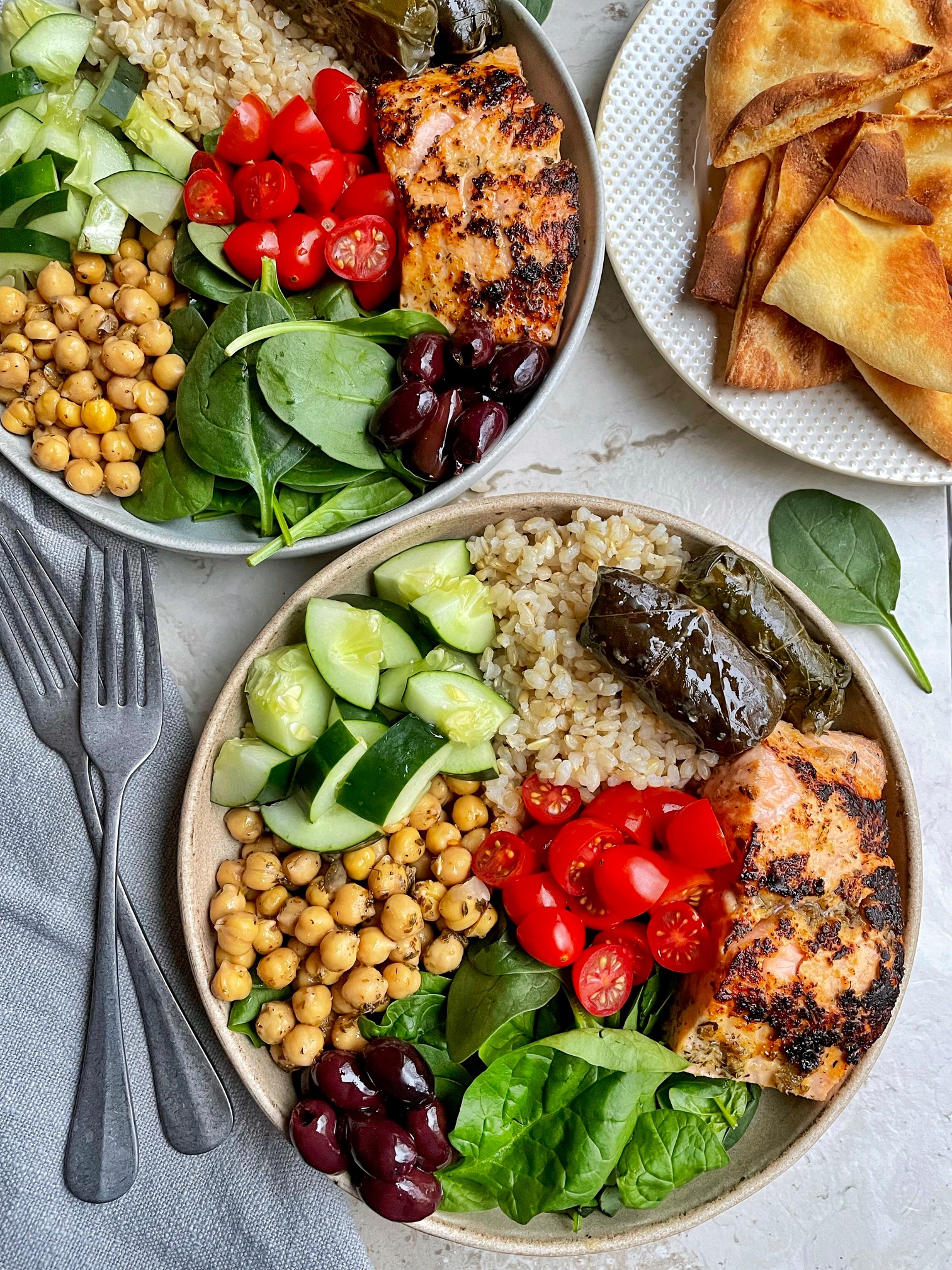 a wider shot of two Greek salmon bowls with a side of pita