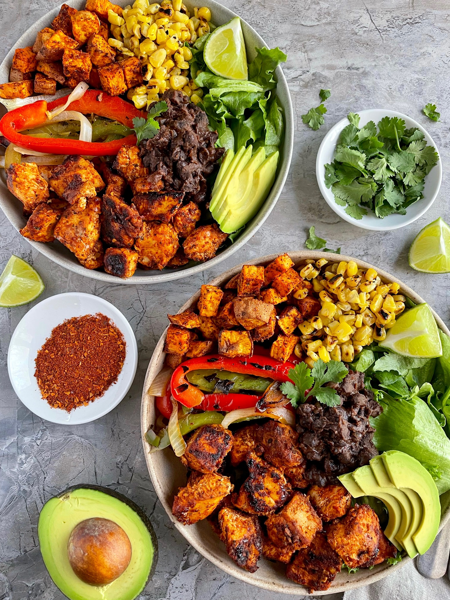 Two Southwest Chicken bowls with bowls of garnishes and half an avocado around them