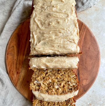 oat flour carrot cake loaf with cinnamon cream cheese frosting on a cutting board with three slices cut.