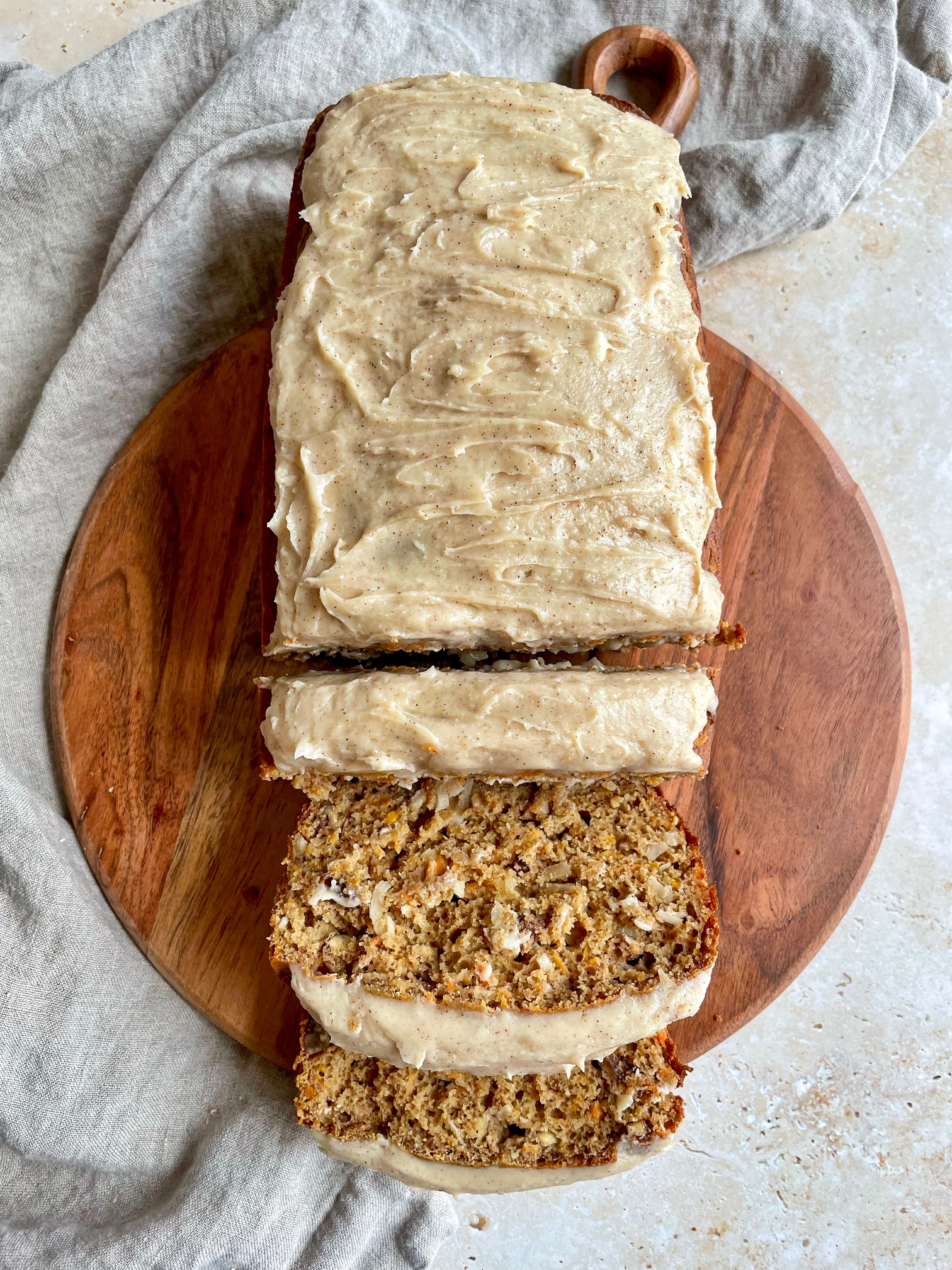 oat flour carrot cake loaf with cinnamon cream cheese frosting on a cutting board with three slices cut.