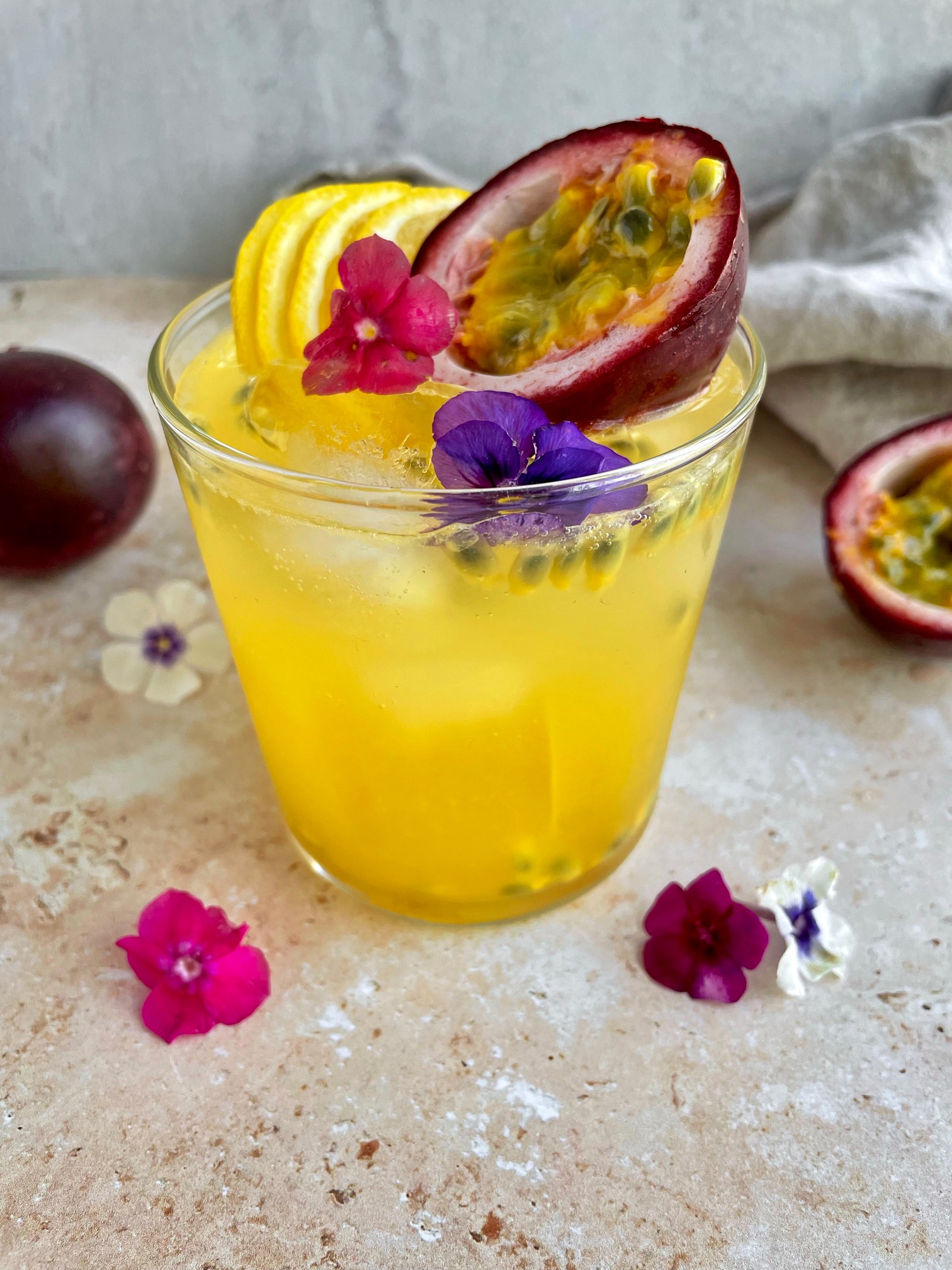 the completed passion fruit cocktail garnished with lemon slices, passion fruit and edible flowers.