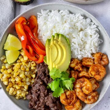 a close up of one of the shrimp burrito bowls with an avocado half next to it.