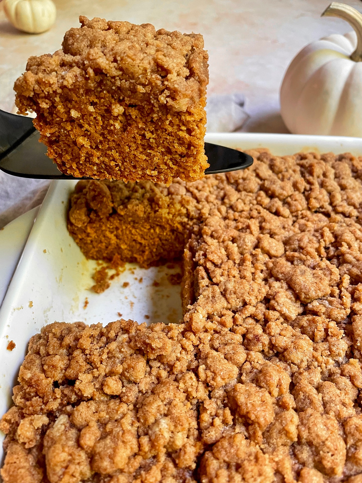 lifting a piece of pumpkin coffee cake out of the baking dish.