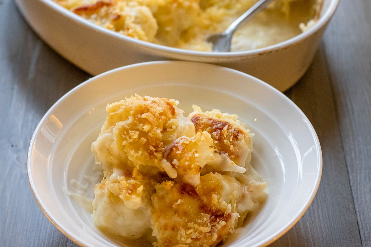 a bowl of cheesy baked cauliflower with the pan in the background.