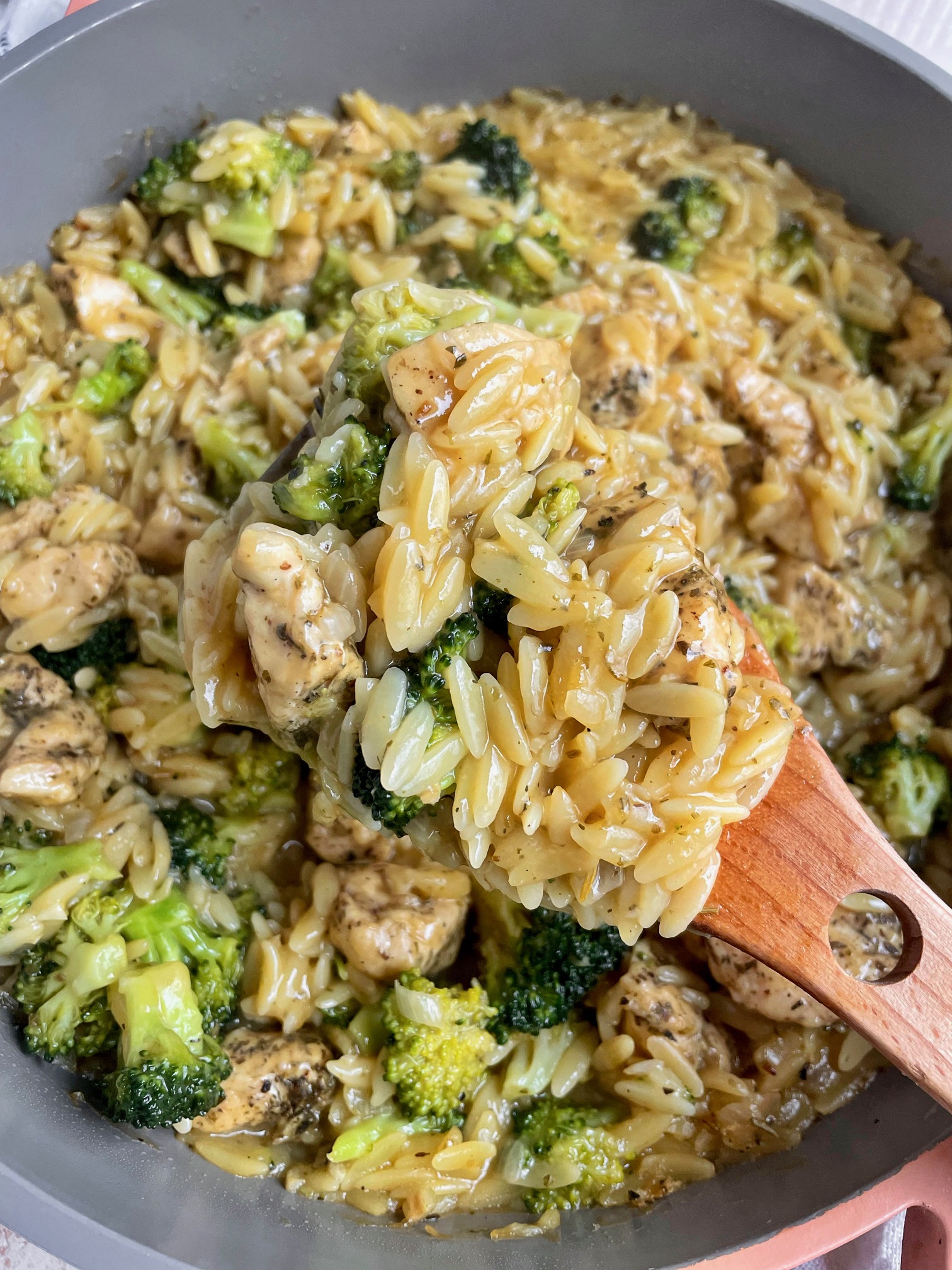 Some broccoli cheddar chicken orzo close up on a wooden spoon to show detail.