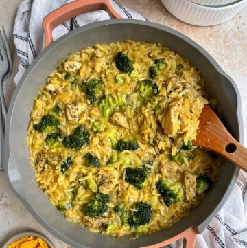 The broccoli cheddar chicken orzo in the skillet with bowls and forks next to it.