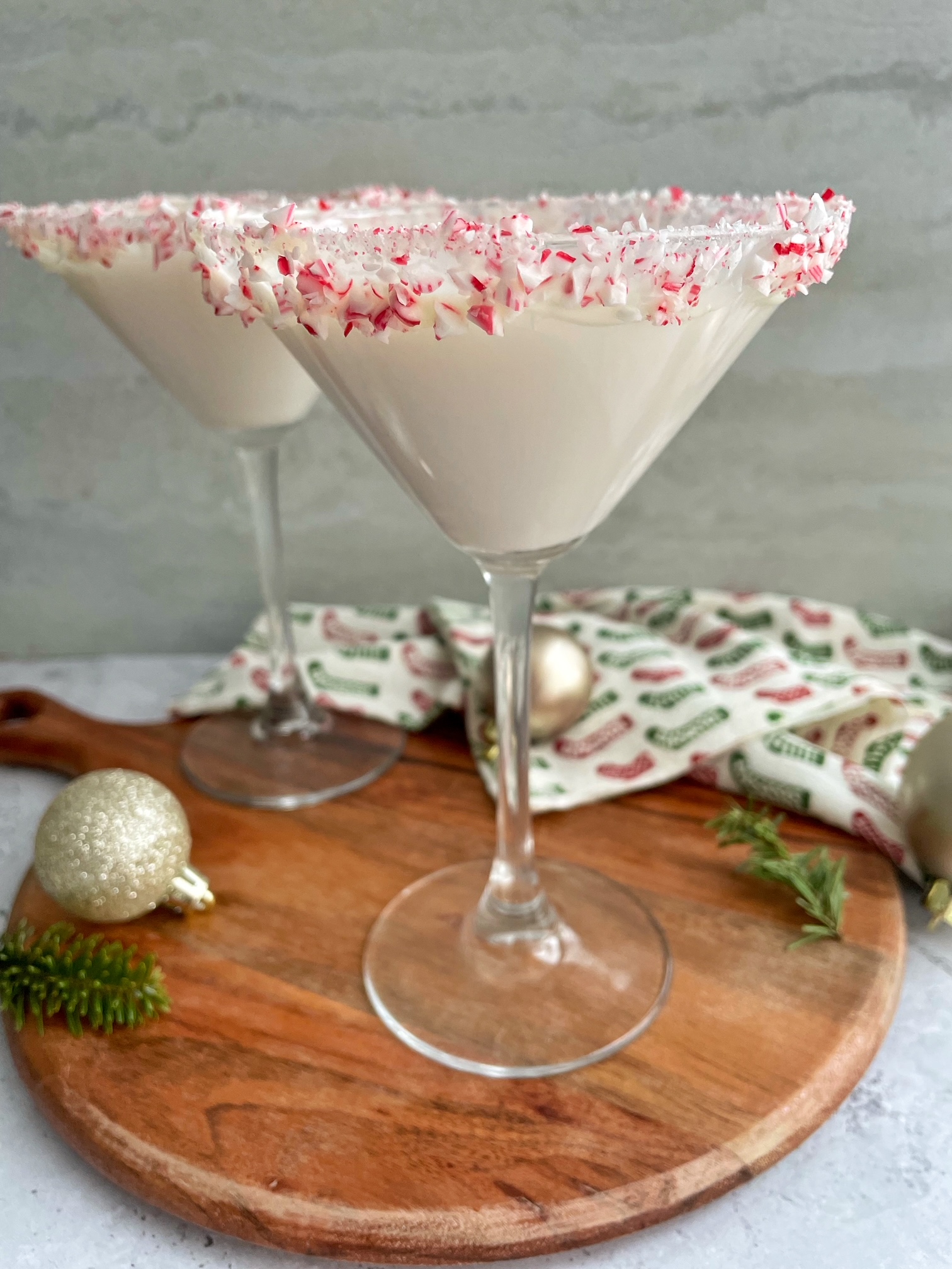 Two white chocolate peppermint martinis on a wooden board.