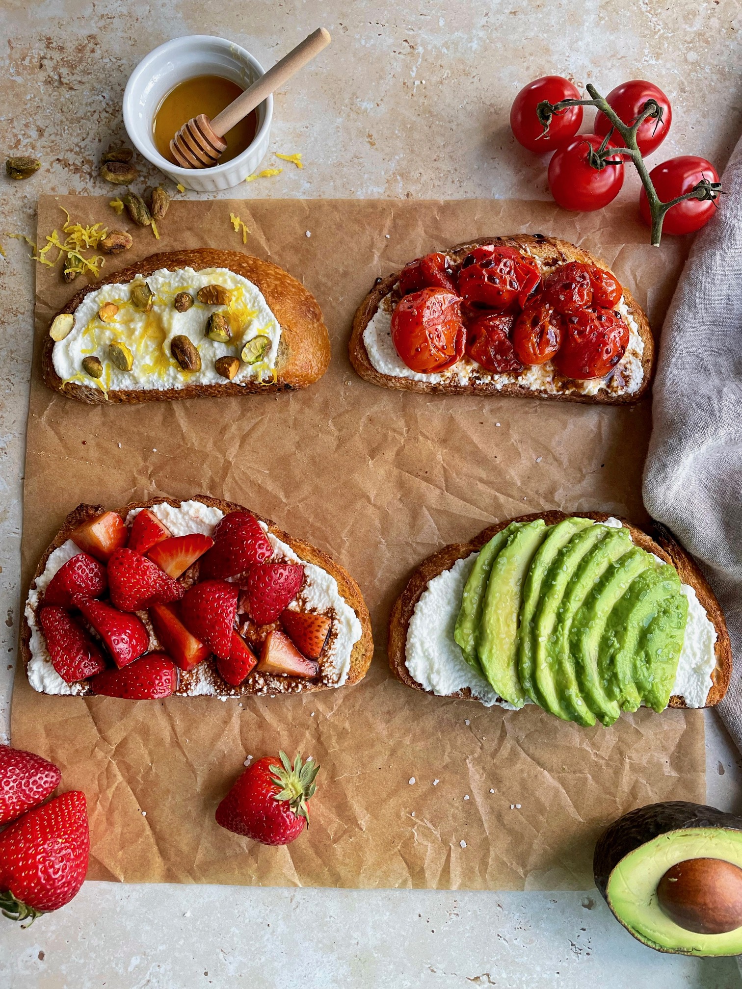 The 4 ricotta toasts on a piece of parchment paper with various ingredients surrounding them.