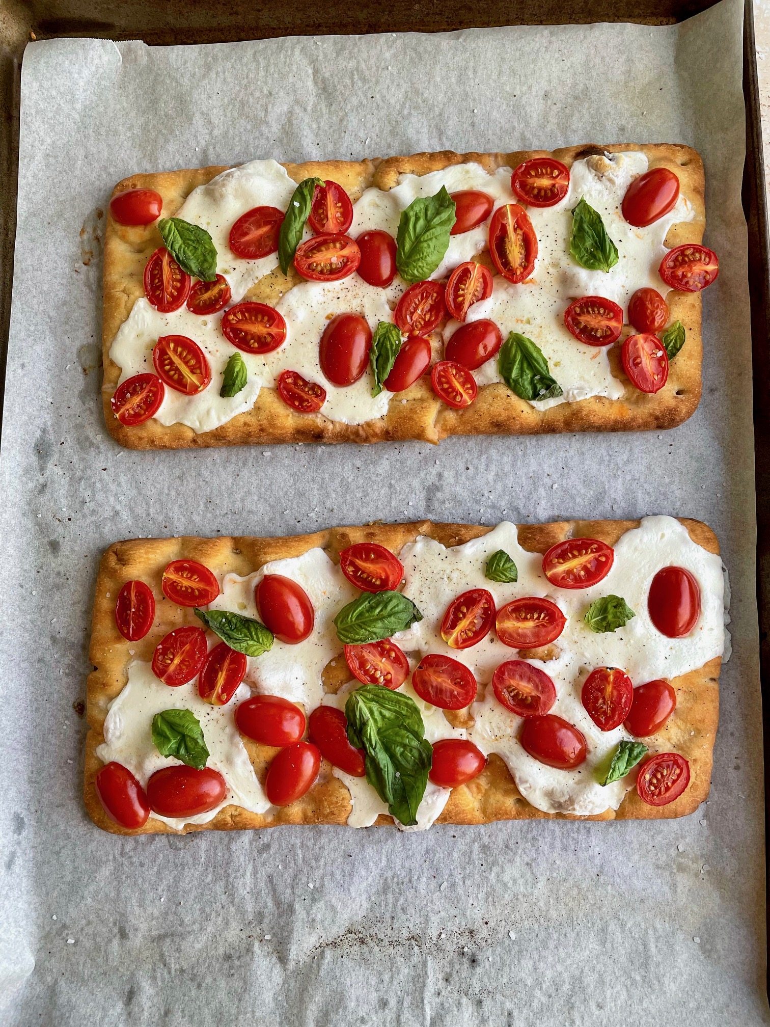 Caprese flatbreads finished baking with basil added before cutting into pieces and adding balsamic glaze.