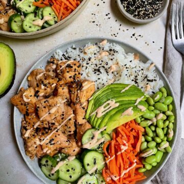 A close up of an Asian salmon rice bowl with a small bowl of furikake seasoning next to it.