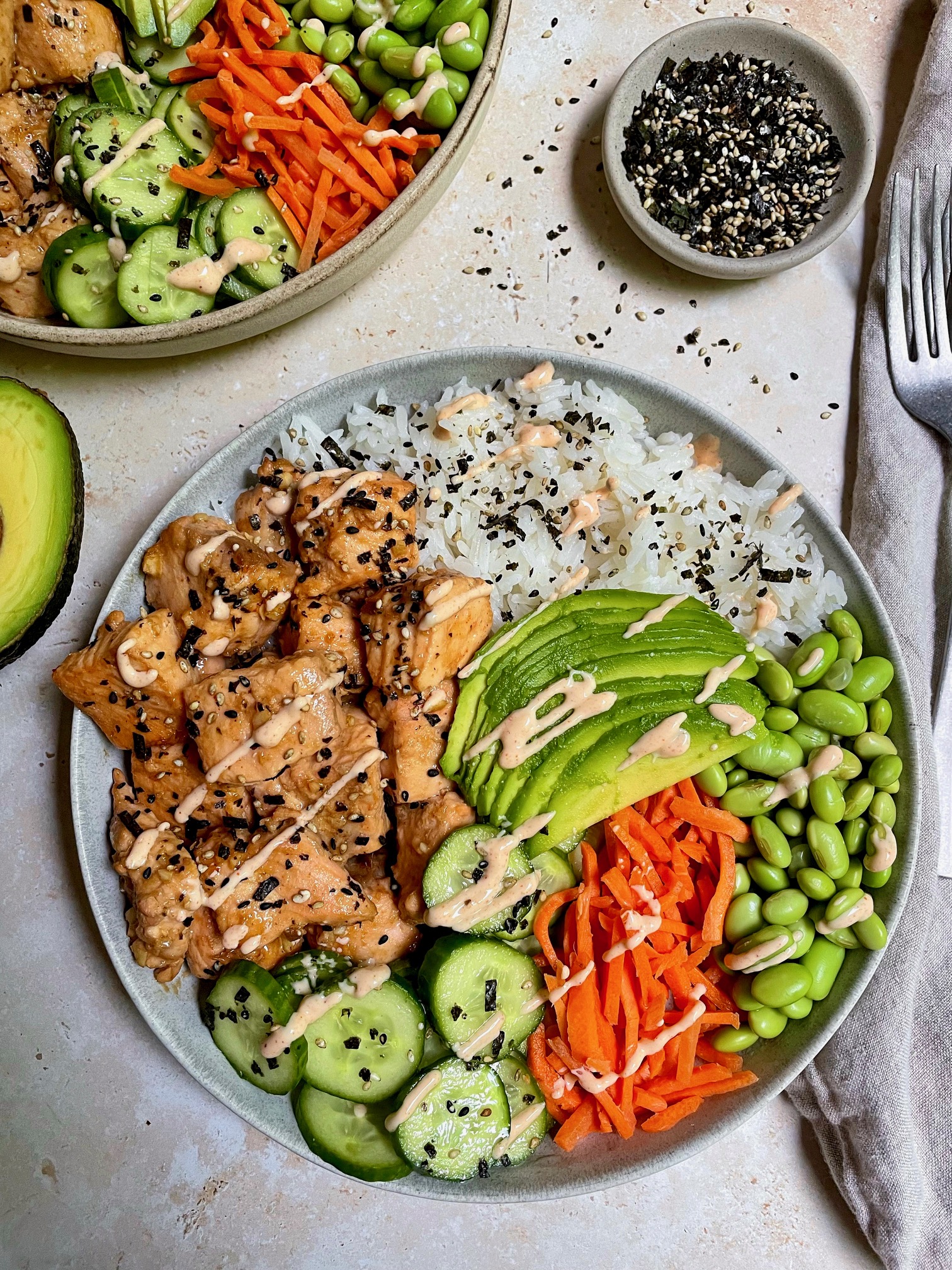 A close up of an Asian salmon rice bowl with a small bowl of furikake seasoning next to it.