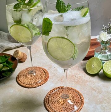 Two hugo spritz on coasters with lime wedges around them.