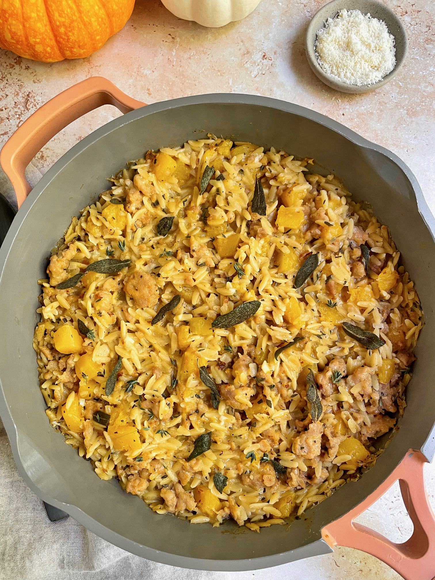 The finished butternut squash sausage orzo in the pan with a small bowl of parmesan cheese next to it.