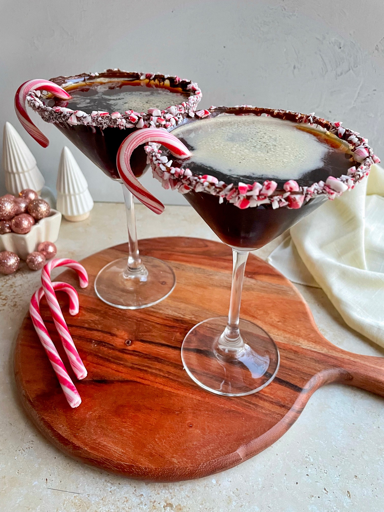 Peppermint espresso martinis on a wooden cutting board with candy canes next to them.
