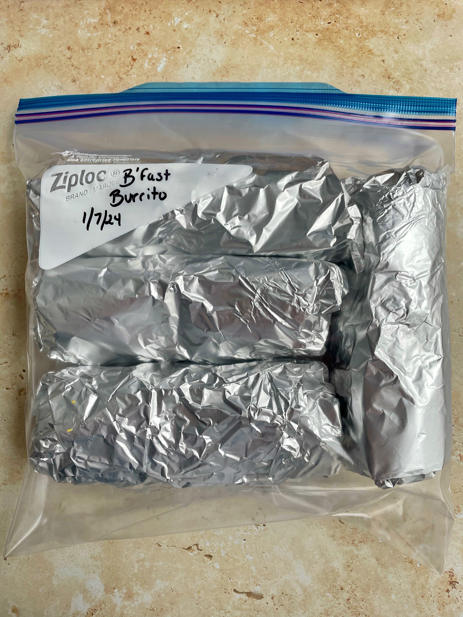 Breakfast burritos wrapped in aluminum foil and in a plastic bag ready for the freezer.
