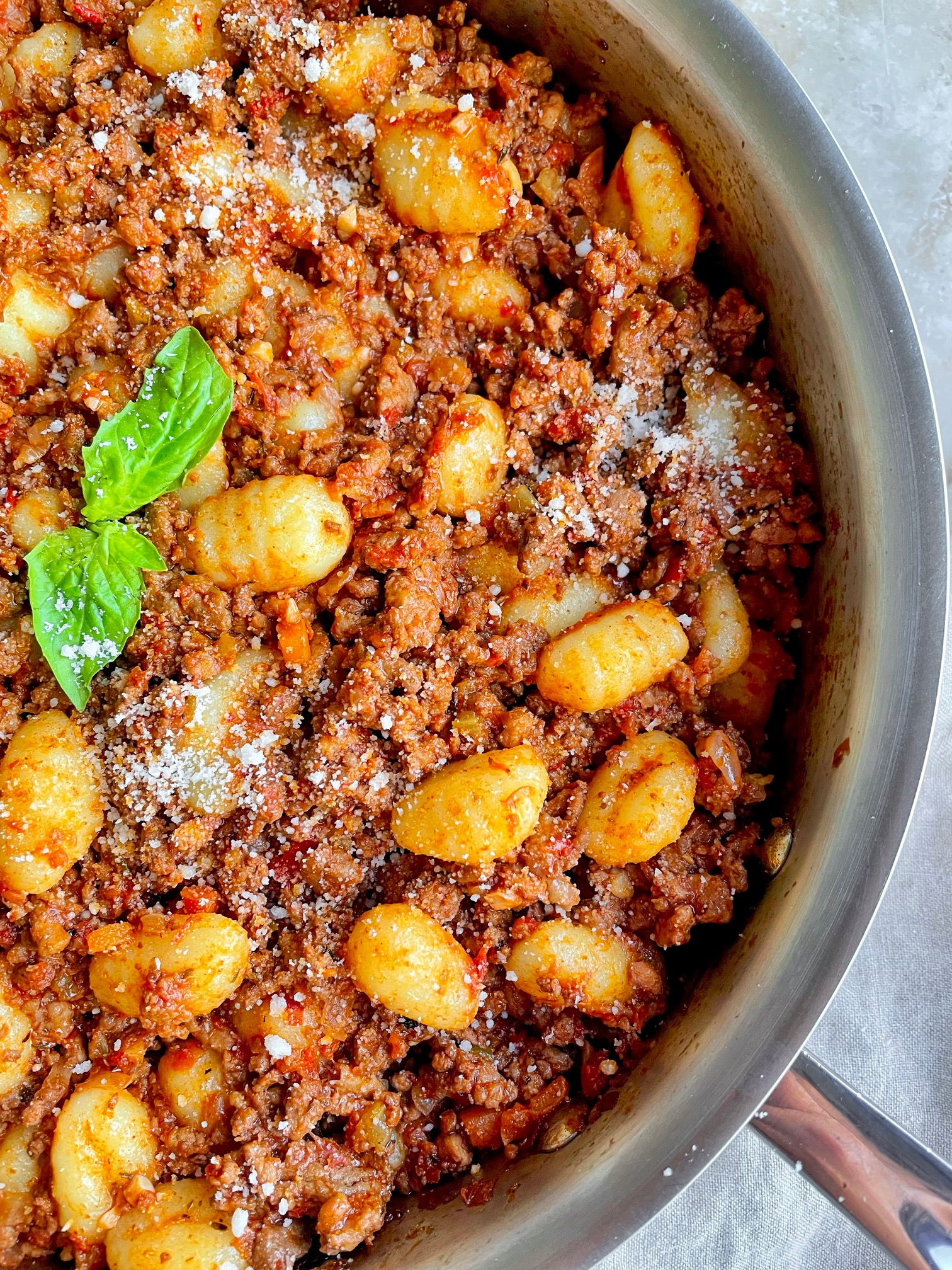 A close up of the gnocchi bolognese in the pan with a basil garnish.