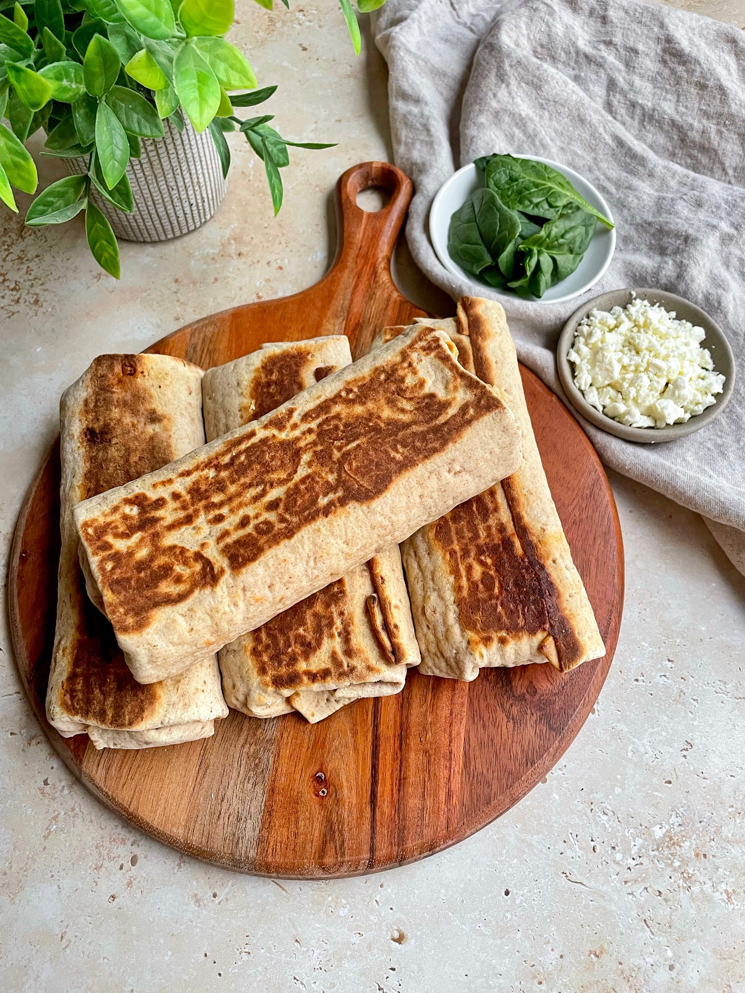 Four egg white wraps sitting on a round cutting board with bowls of ingredients and a towel next to it.