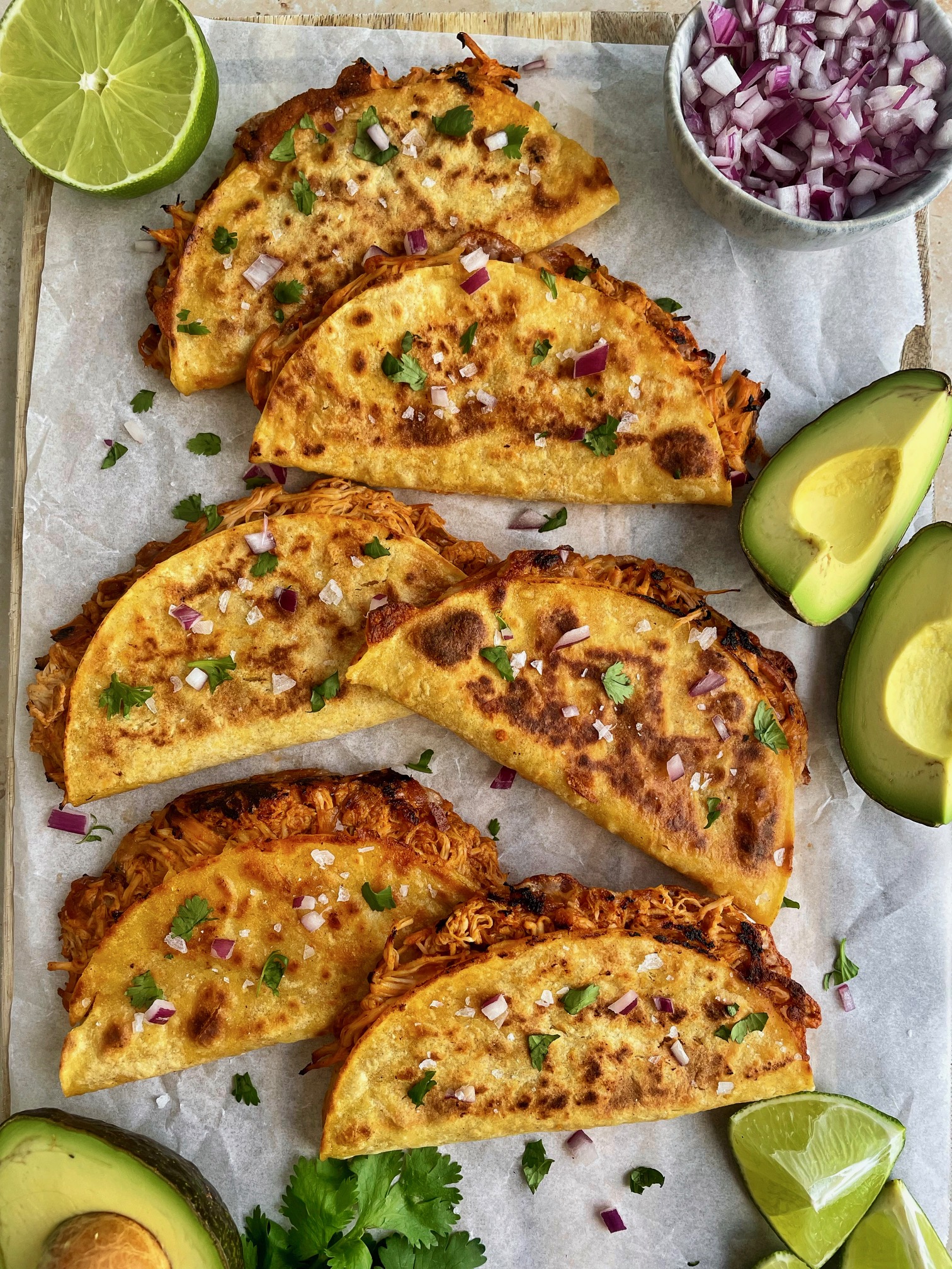 6 crispy salsa chicken tacos on a cutting board with garnishes around them.