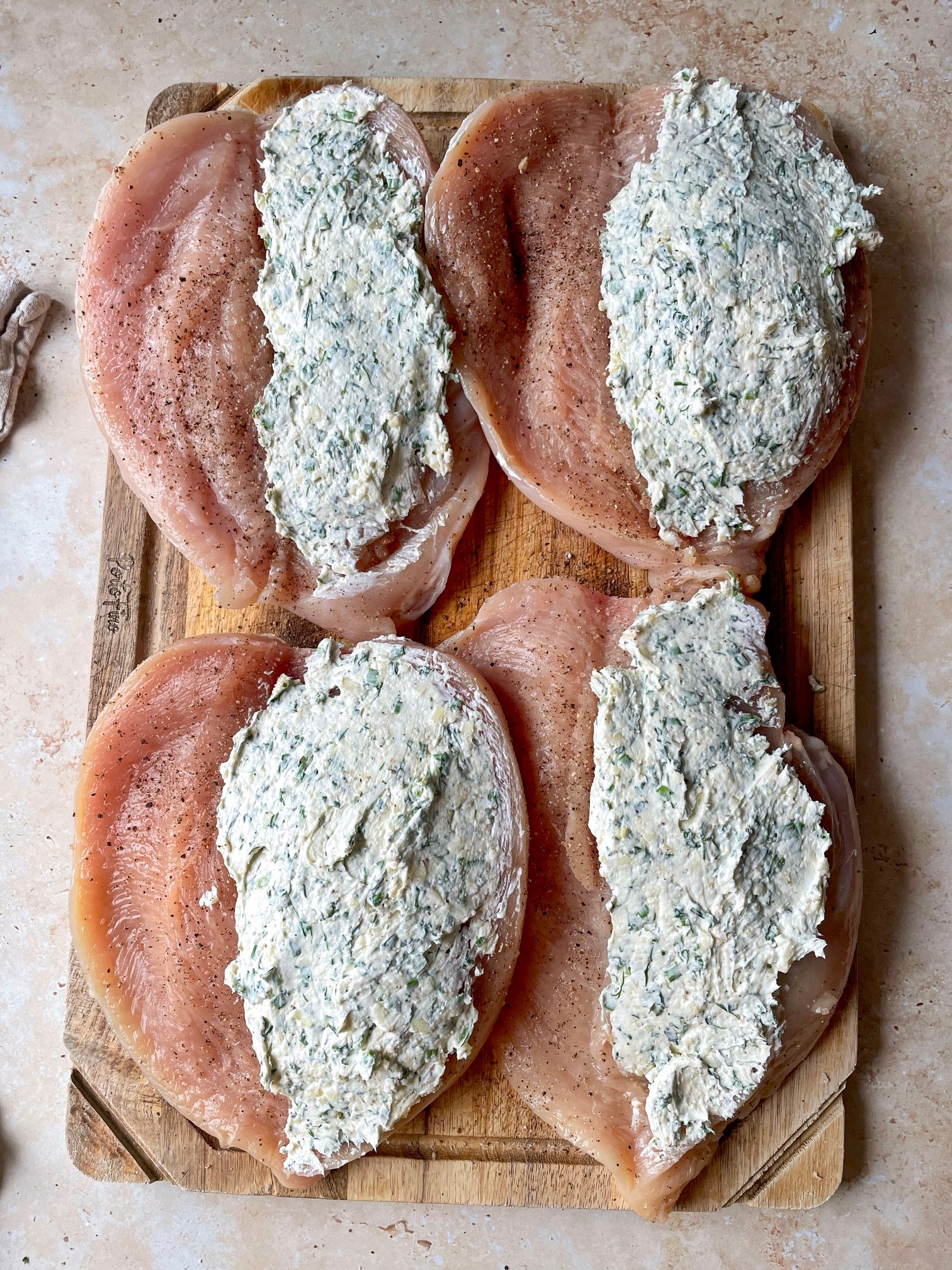 Four chicken breasts filleted on a cutting board with filling covering one half of each. 