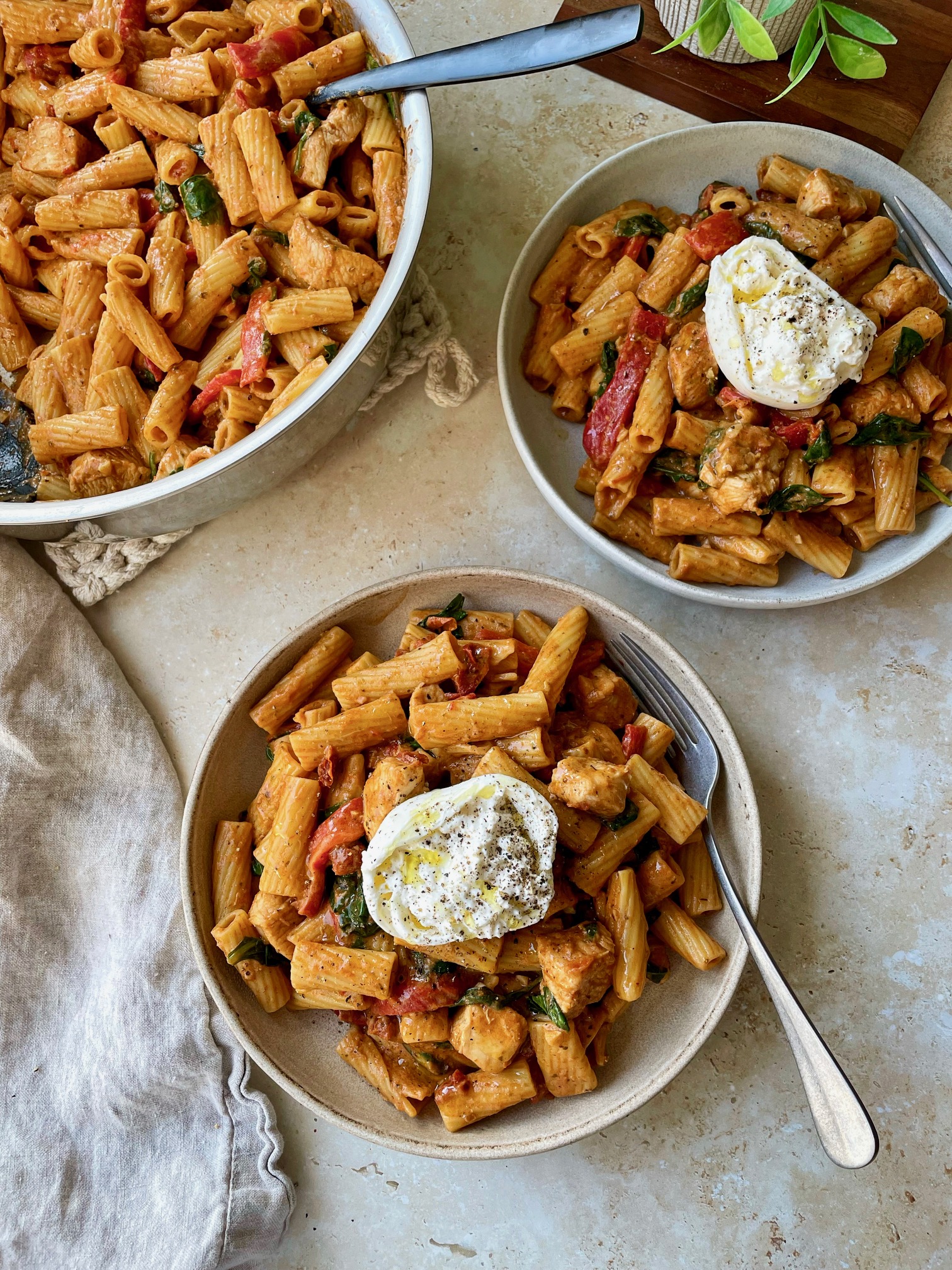 Two bowls of creamy tomato pesto pasta with chicken topped with burrata halves.