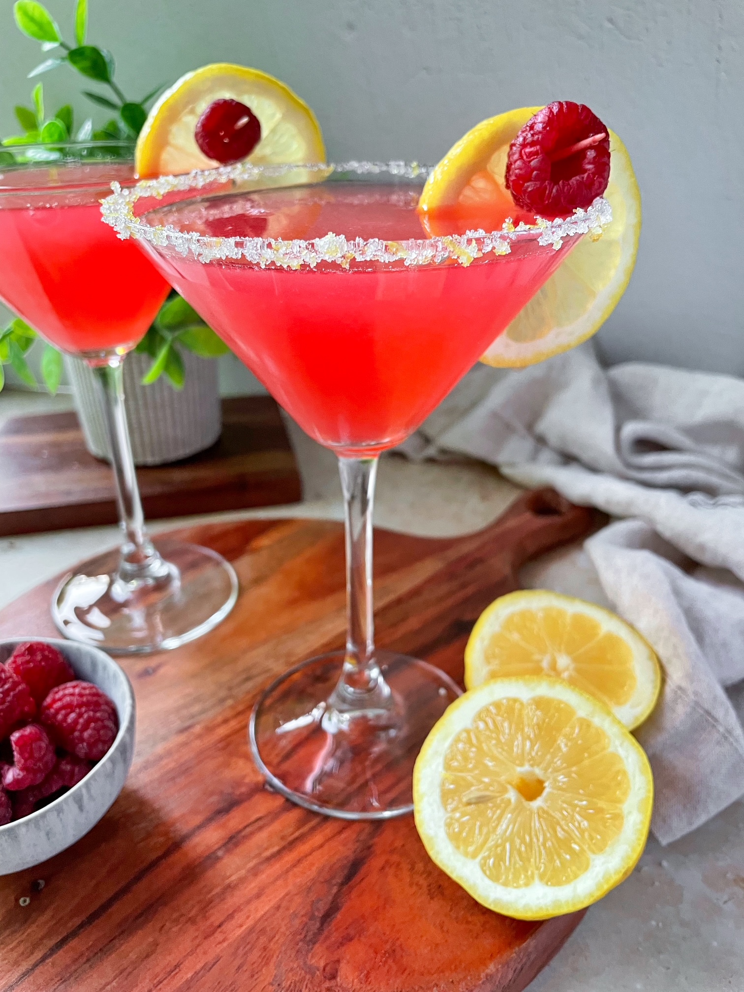 Raspberry lemon drop martini in a martini glass with a sugar rim garnished with a lemon slice and raspberry. 