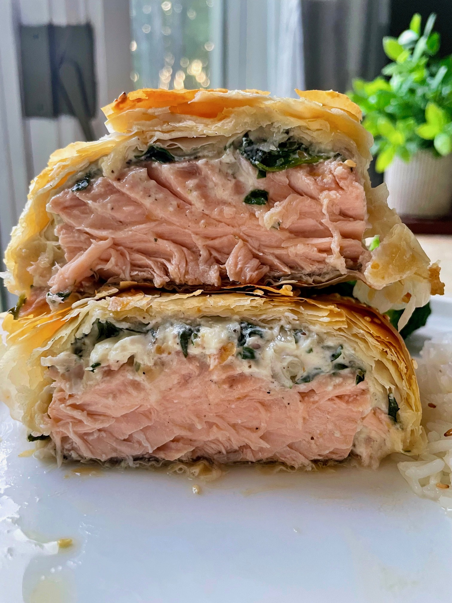 Spinach feta phyllo wrapped salmon cut in half with the two halves stacked on top of each other to show the layers.