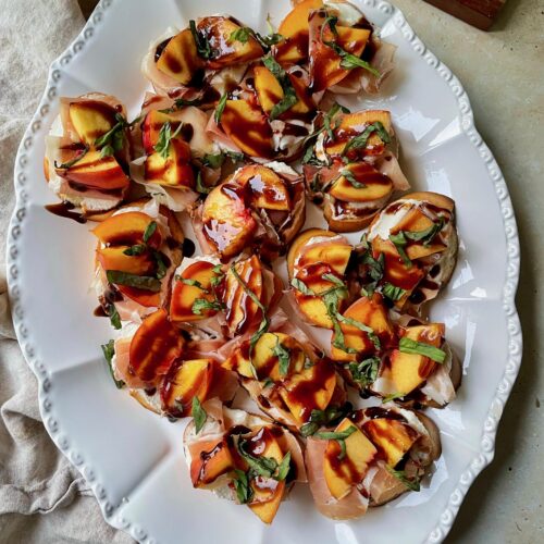 A platter of peach, ricotta and prosciutto crostini drizzled with balsamic glaze.