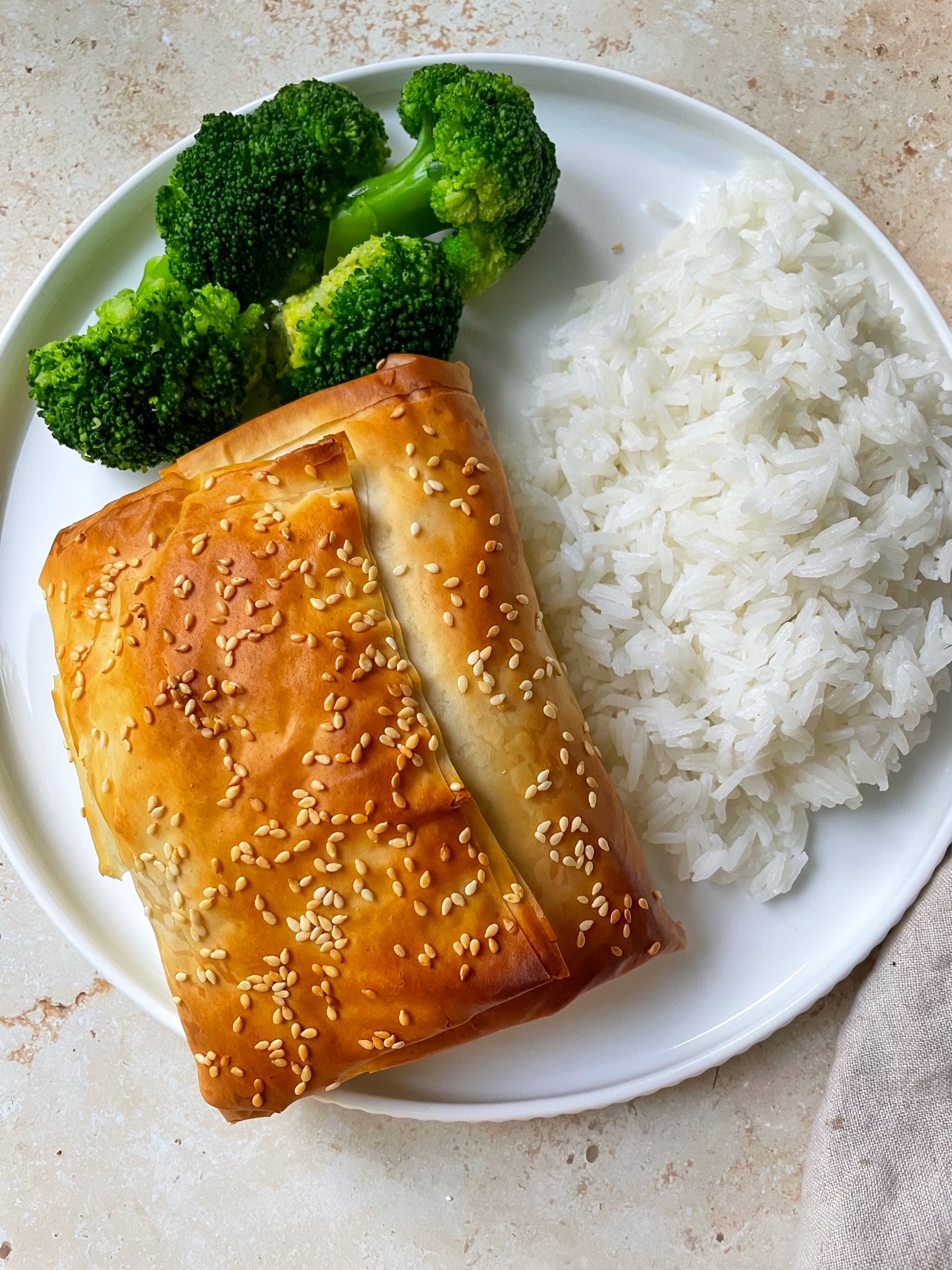 An overhead shot of a plate with a spinach feta phyllo wrapped salmon topped with sesame seeds with a side of rice and broccoli.