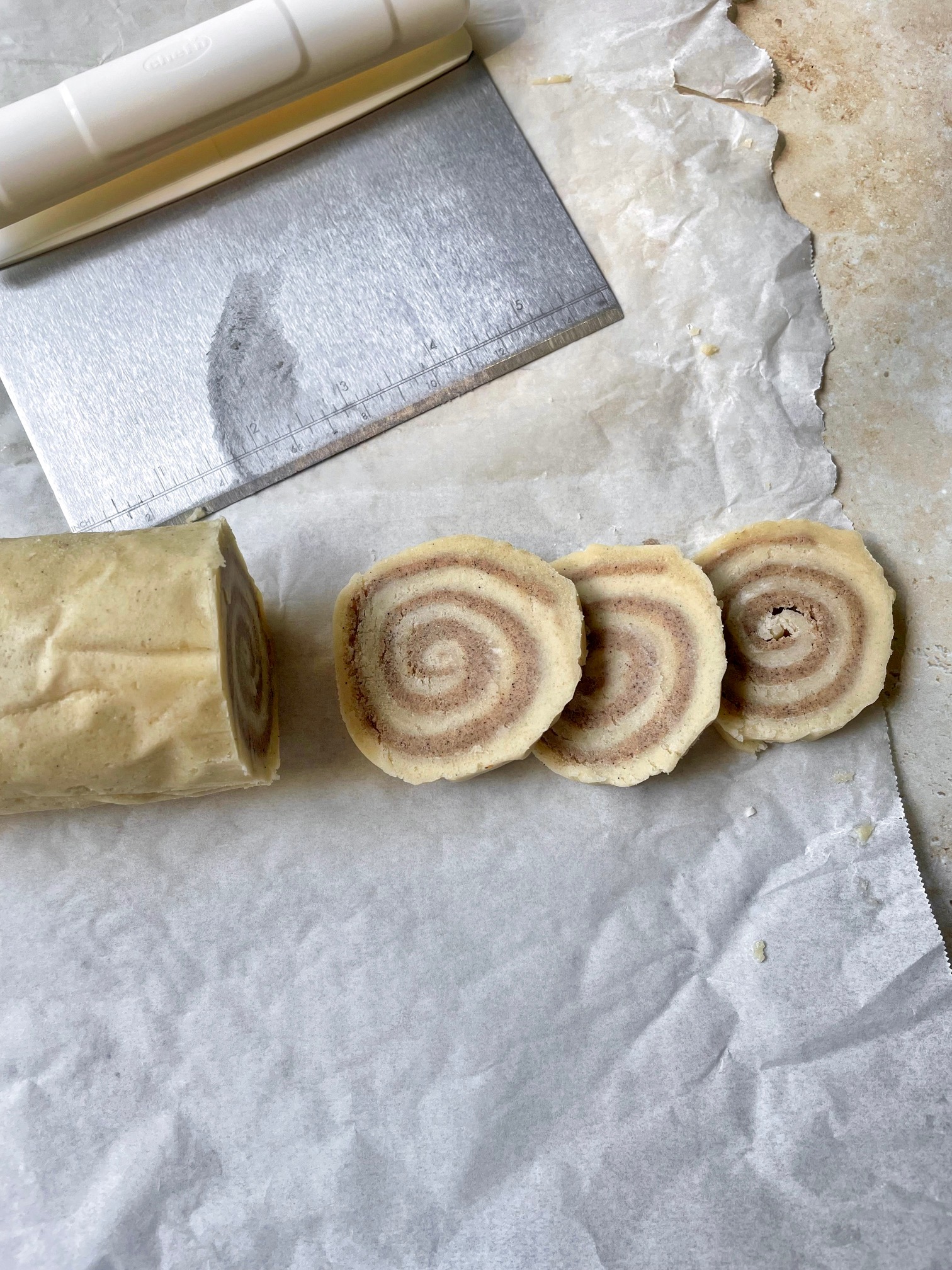 Cookie dough log with three slices next to it and a bench scraper used to cut the slices.