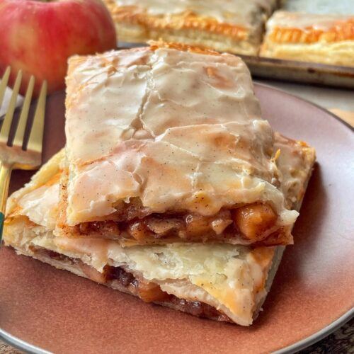 Two slices of apple cinnamon strudel on top of each other on a plate with a fork.