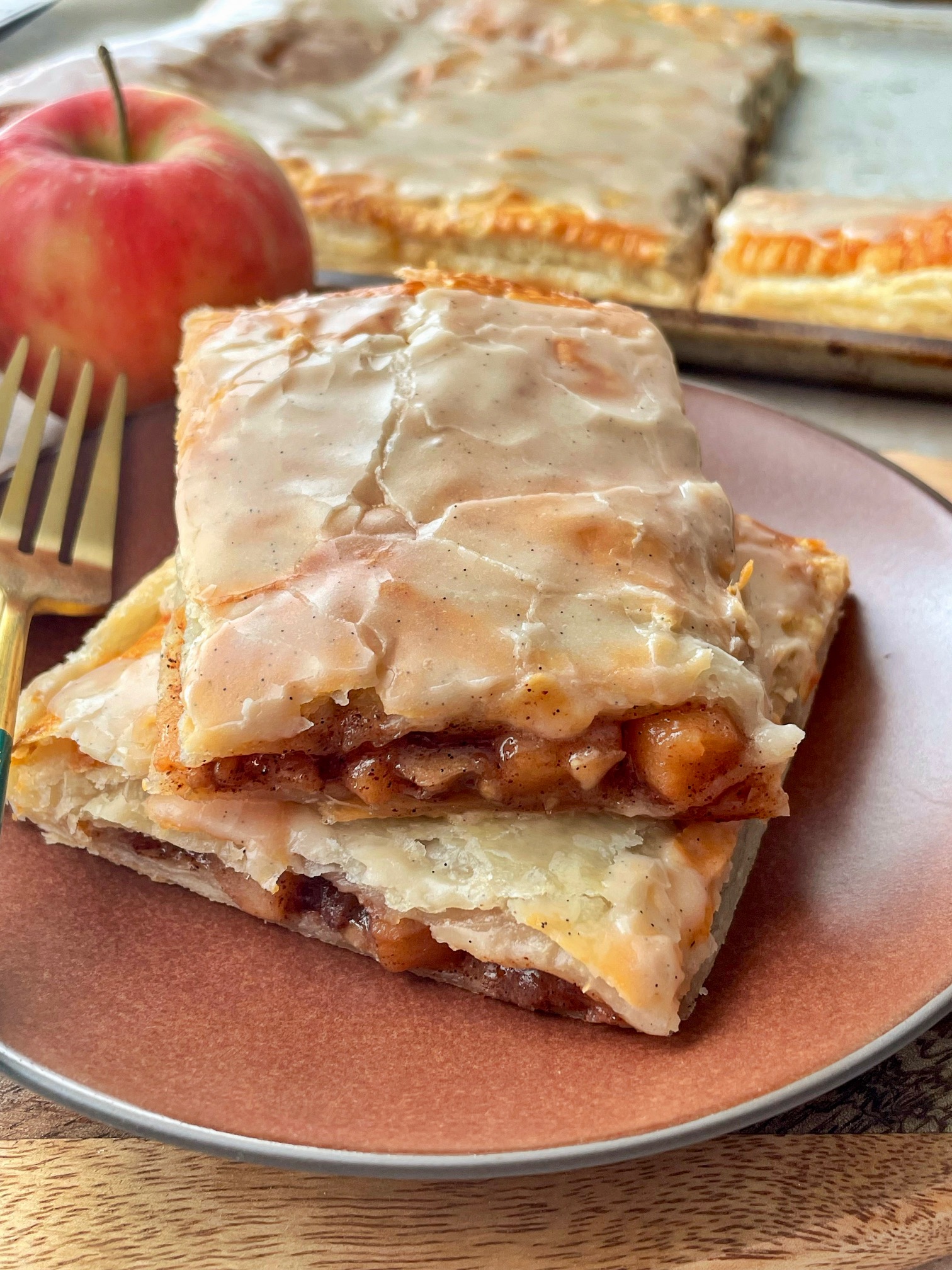 Two slices of apple cinnamon strudel on top of each other on a plate with a fork.