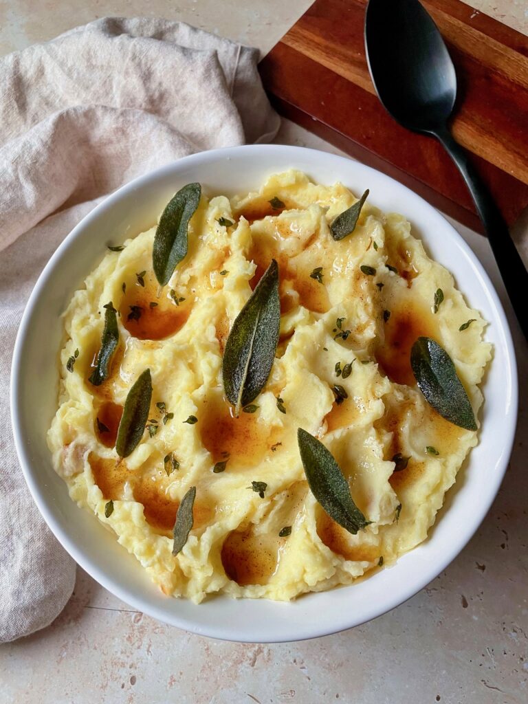 Brown Butter Roasted Garlic Mashed Potatoes in a serving dish topped with crispy sage and thyme.