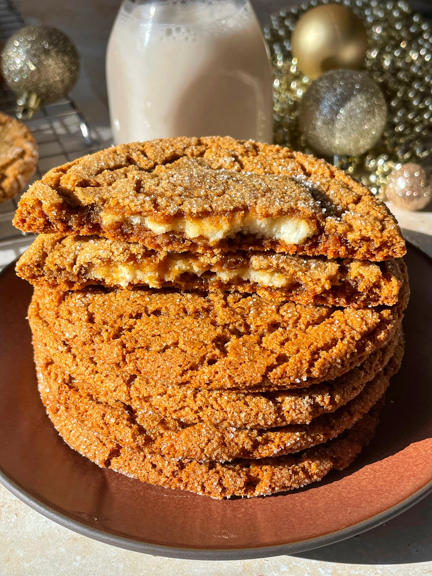 A stack of four gingerbread cookies with a fifth broken in half to show the inside filling.