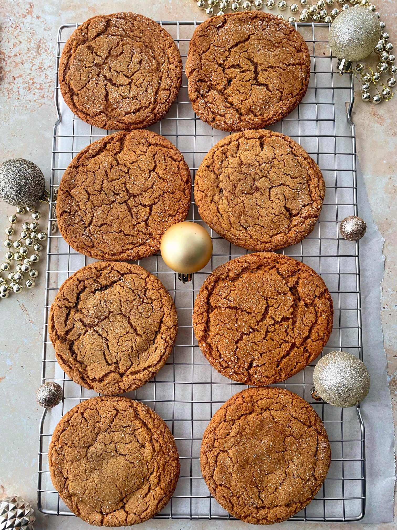 A cooling rack with eight cheesecake stuffed gingerbread cookies on it and various Christmas ornaments around it.