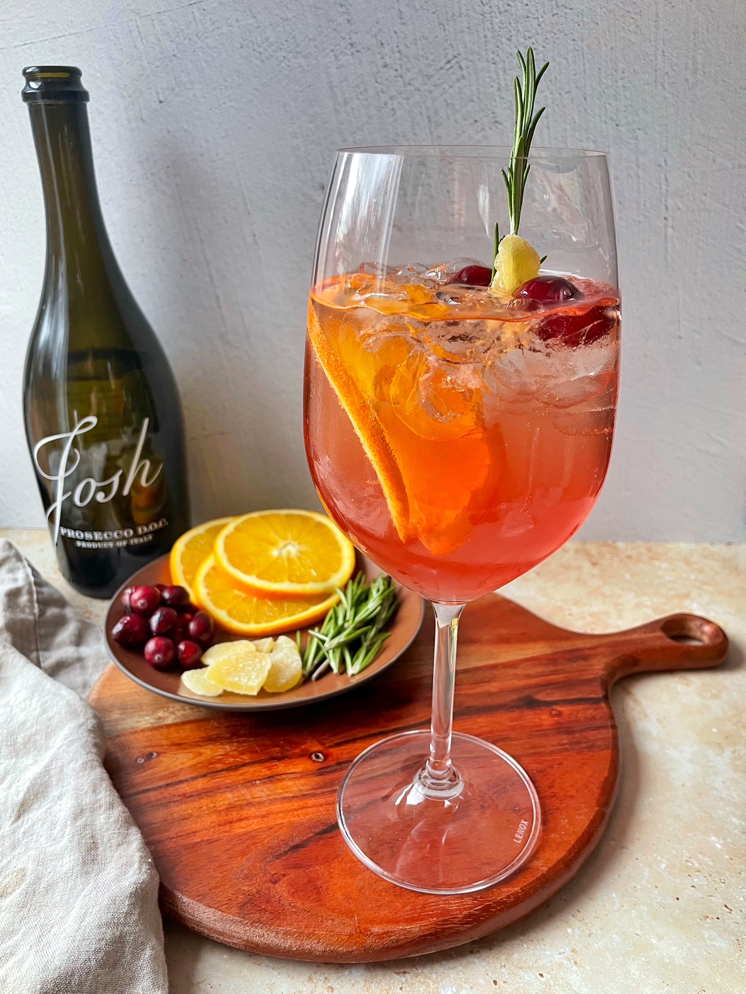 A spritzer on a cutting board with garnishes and a bottle of prosecco.