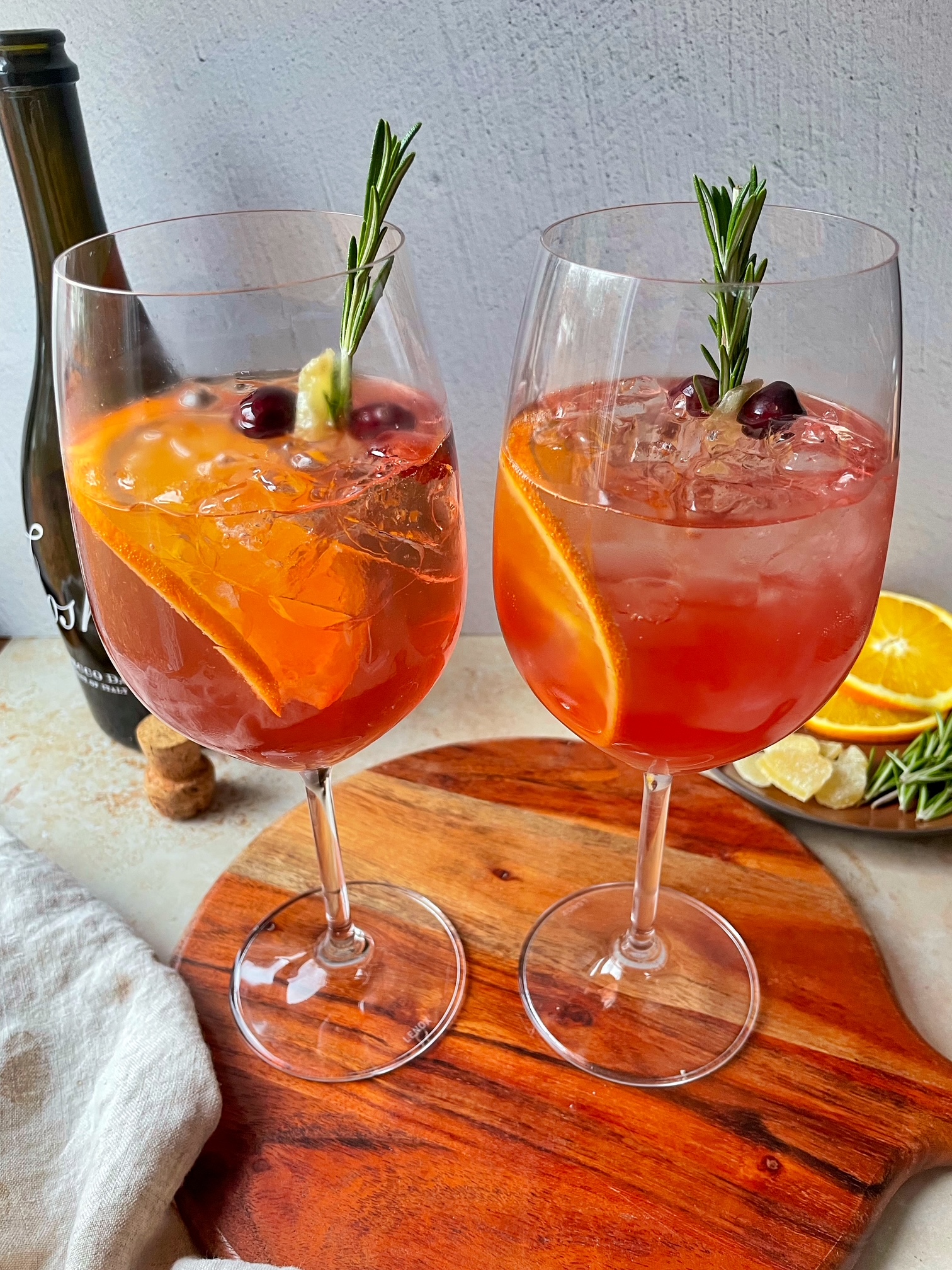 Two cranberry ginger spritzers topped with garnishes on a wooden cutting board.