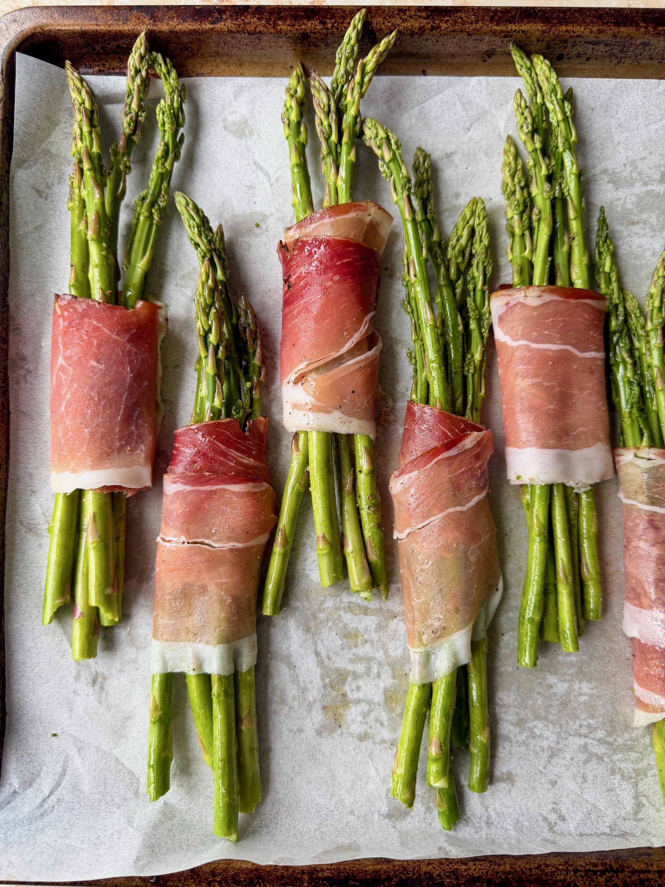 Prosciutto wrapped asparagus on a baking sheet before going in the oven.