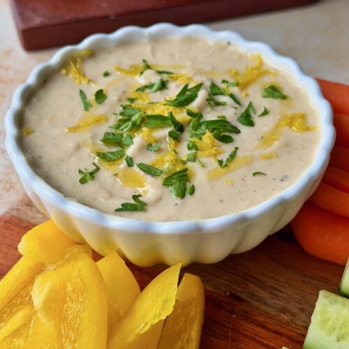 White bean dip topped with lemon zest and parsley served with dippers.