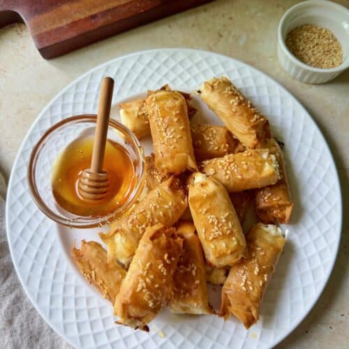 A plate of feta phyllo rolls with a ramekin of honey for serving.