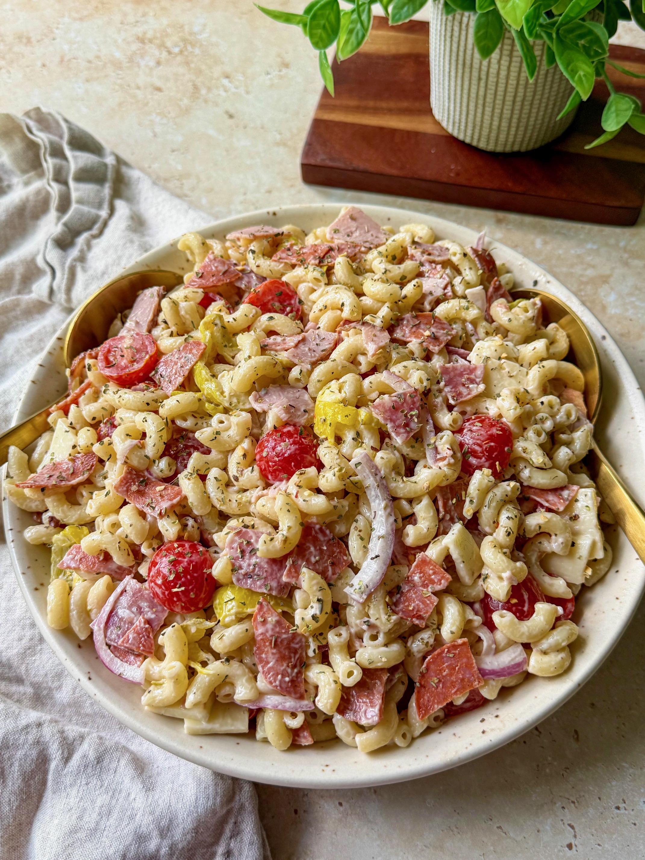 Italian grinder pasta salad in a serving bowl with serving spoons.