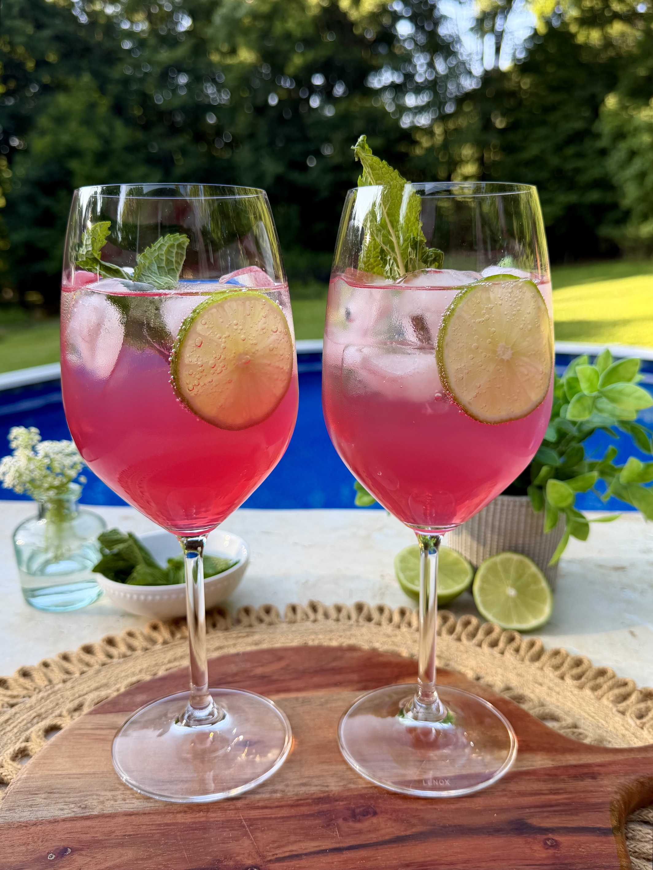 Two glasses of sarti spritz garnished with lime and mint. Photographed outside.